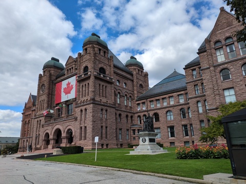 [Façade de l'édifice de l'Assemblée législative de l'Ontario, portant un énorme drapeau canadien]